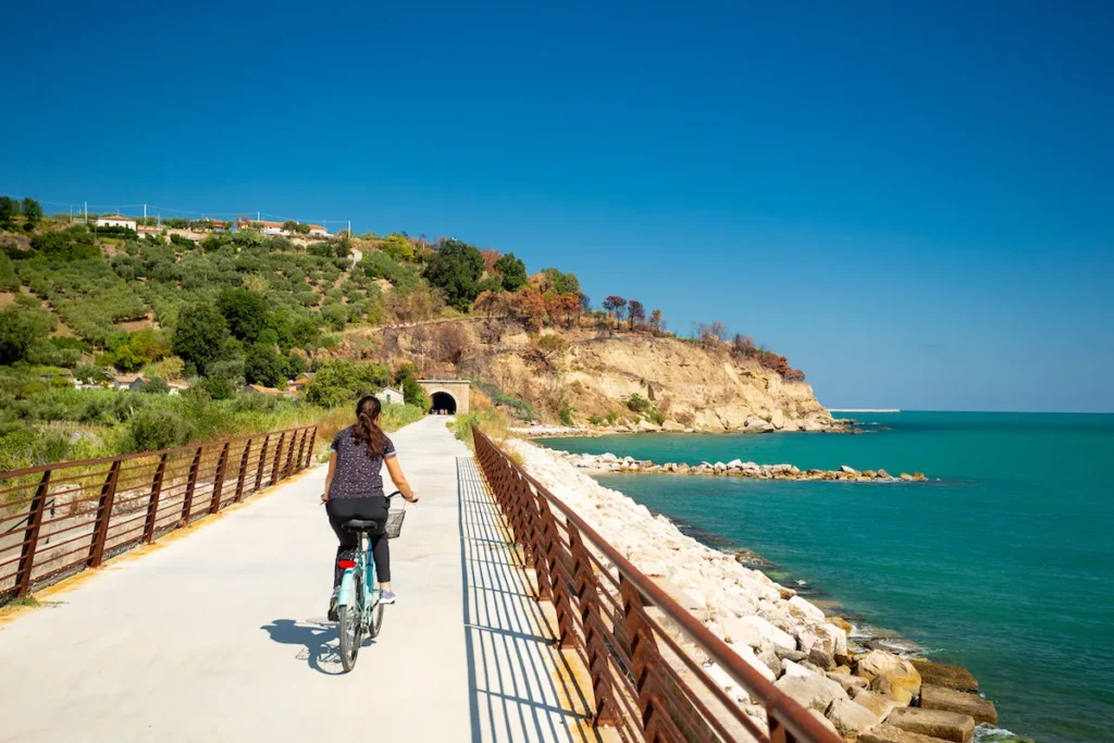 Donna in bicicletta su pista ciclabile costiera con mare turchese